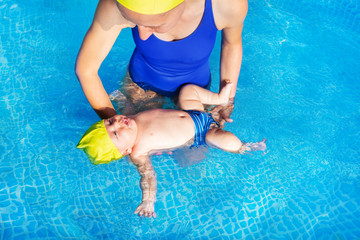 Mother teach small baby infant to floating on back in indoor swimming pool