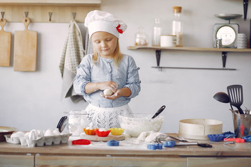 Child in a kitchen. Little girl with a dough. Kid in a blue shirt and white shef hat. Girl with cupcake shape.