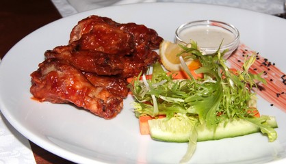 Sweet chicken wings with vegetables and rukala. Food on a white plate with milk sauce.