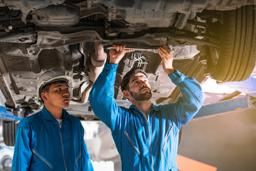 Mechanic in blue work wear uniform inspects the car bottom with a wrench with his assistant....