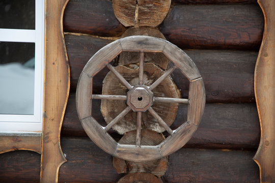 A wooden wheel hangs on the wall. Rural surroundings.