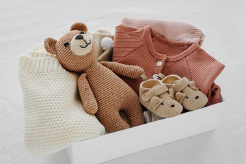 Box with baby stuff and accessories for newborn on bed. Gift box with knitted blanket, clothes,...