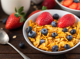 Granola chips with blueberries and raspberries in white bowl in dark wooden desk.