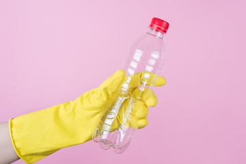 Plastic recycling concept. Cropped close up side profile view photo of hand in yellow glove holding an empty bottle isolated over background
