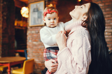 Elegan family at home. Beautiful brunette in a pink sweater. Little girl with red bow