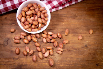 Nuts in a white bowl on a wooden background next to a checked towel