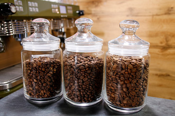 Glass bank with coffee grains costs on a table on a wood background
