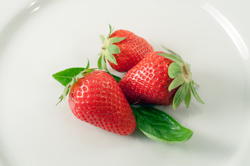 strawberries and basil leaves isolated on a white plate. healthy food. Simplicity, vitality.