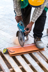 Construction work on pavement. Installation of concrete paver blocks on the sidewalk. A worker makes measurements, mark and cut build materials by a disc cutter.