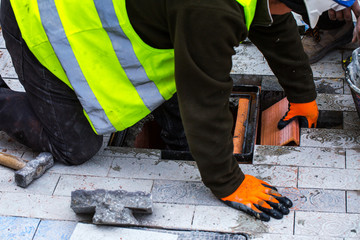 Construction work on pavement. Installation of concrete paver blocks on the sidewalk. Workers do the installation of the well hatch for engineering communications in the pavement.