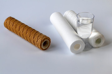 The water filter is two units and a cartridge that requires replacement. Near a glass of clean water. White background, no isolation. Close-up