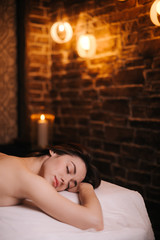 Obraz na płótnie Canvas Close-up of face of beautiful naked girl with perfect body is lying on massage table waiting for massage in light massage room. Concept of luxury professional massage.