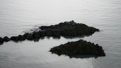 Small black rocky basalt rock island in water in Iceland