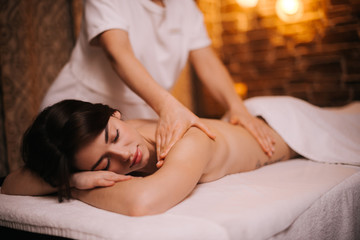 Obraz na płótnie Canvas Portrait of young relaxed woman lying on massage table, receiving back and shoulder massage at the spa salon. Concept of luxury professional massage. Concept of body care.