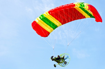 Motorized paraglider in flight overhead in blue sky 