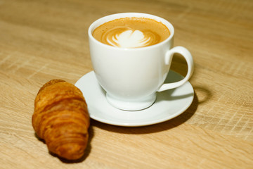 A cup of coffee with heart pattern in a white cup on wooden background