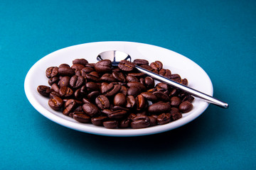 White espresso cup and saucer with brown coffee on a teal blue surface with beans and spoon.