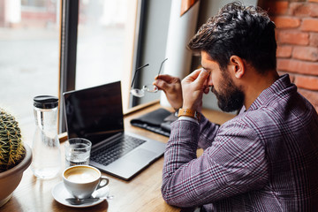 Tired student male in eyeglases at cafeteria, using laptop