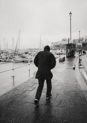 A man battles against wind and rain alongside Ramsgate Royal Harbour on a cold winter day. In...