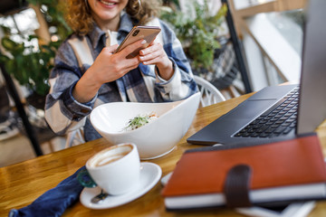 Cropped image, young woman in casual wear make food photo in modern cafe terrace with cup of coffee and salade
