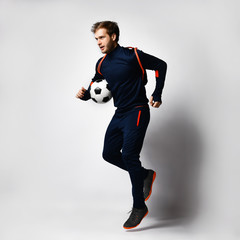 Soccer player in blue tracksuit, colored sneakers and backpack. He is running, holding ball, posing...