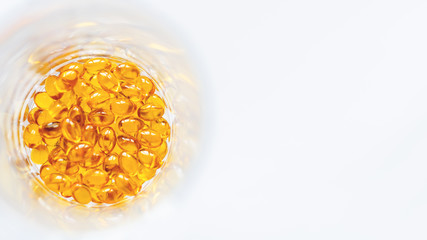 Orange pills inside glass jar. Top view on medicine capsules. White background with copy space.