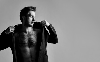 Obraz premium black and white photo of man in black classic suit on naked body. He is straightening his jacket, posing against gray background. Close up