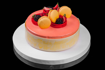 Delicious festive cake decorated with berries and pink icing on a white dish. Black background. Close-up.