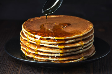 Pancakes with sweet syrup on a wooden background, sweet flour dessert with syrup, traditional...