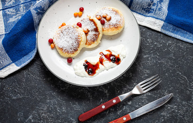 Cottage cheese pancakes on a dark stone background. Syrniki with sour cream. Homemade food.