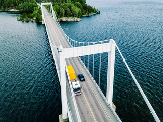 Aerial view of white suspension bridge with truck cargo car crossing over blue lake in Finland