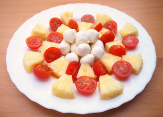 delicious tomato, pineapple and mozzarella salad dressed with olive oil and salt, on a white plate and a wooden table