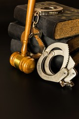 Police handcuffs and books of laws on black background. Wooden gavel and books on wooden table, law concept. Law and order.