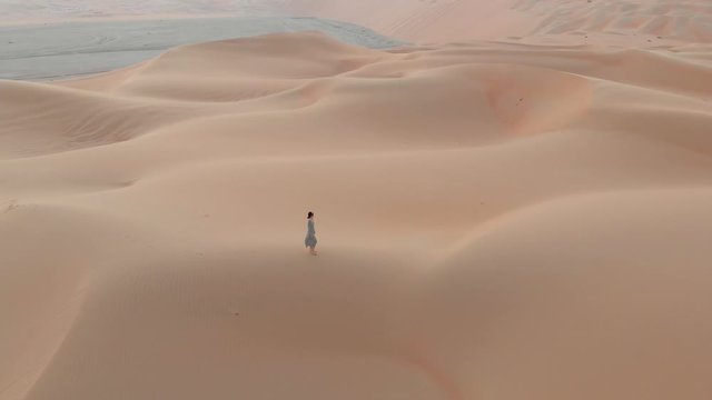 Woman walking on the desert sand dunes aerial view at sunset