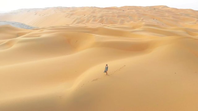 Woman walking on the desert sand dunes aerial view at sunset
