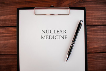 Words nuclear medicine: text written on a shit of paper of notebook on the wooden background. Medical concept.