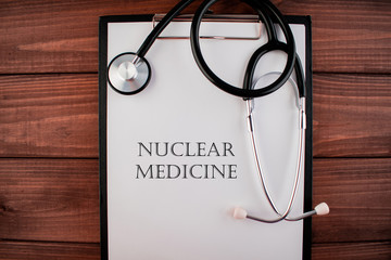 Words nuclear medicine: text written on a shit of paper of notebook with stethoscope on the wooden...