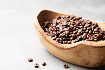 Coffee beans in a wooden bowl made of olive wood on a light gray background. Space for text.