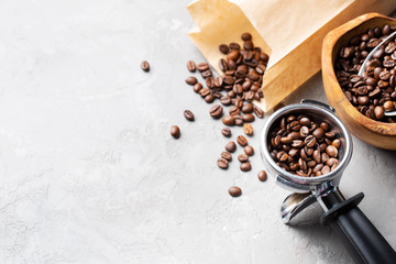 Coffee beans in a wooden bowl made of olive wood, in a paper bag and a metal portafilter on a light gray background. Space for text.