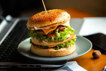 Eating at work place - fast food. burger near laptop. lunch break while you work or sharing online
