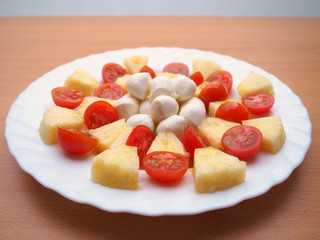 Delicious tomato, pineapple and mozzarella salad dressed with olive oil and salt, on a white plate and a wooden table