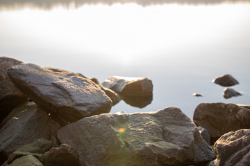Stones on the river bank. The rays of the rising sun are reflected from the water.