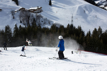 Child, watching rescue action on ski slope, helicopter picking up injured person from ski slope