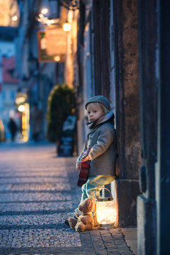 Sweet toddler boy, playing guitar at night in the city with teddy bear toy