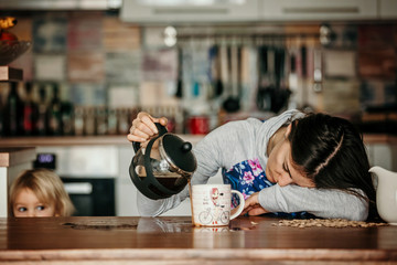 Tired mother, trying to pour coffee in the morning. Woman lying on kitchen table after sleepless...