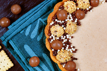 Detail of sweet tart with cheesecake milk chocolate cream filling topped with pralines and chocolate sprinkles on blue kitchen towel