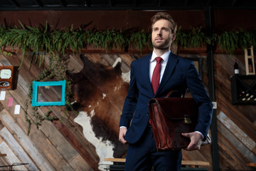 elegant businessman looking away and holding suitcase