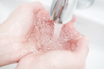 Washing hands under a stream of clean water, in the sink, in the bathroom.