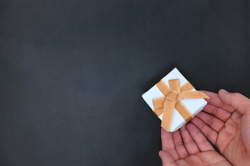 Hands holding white gift in black background. Top view with copy space.