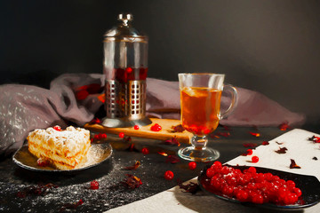 On the table, a mug of tea, a piece of cake and a teapot of tea leaves. On dark background.